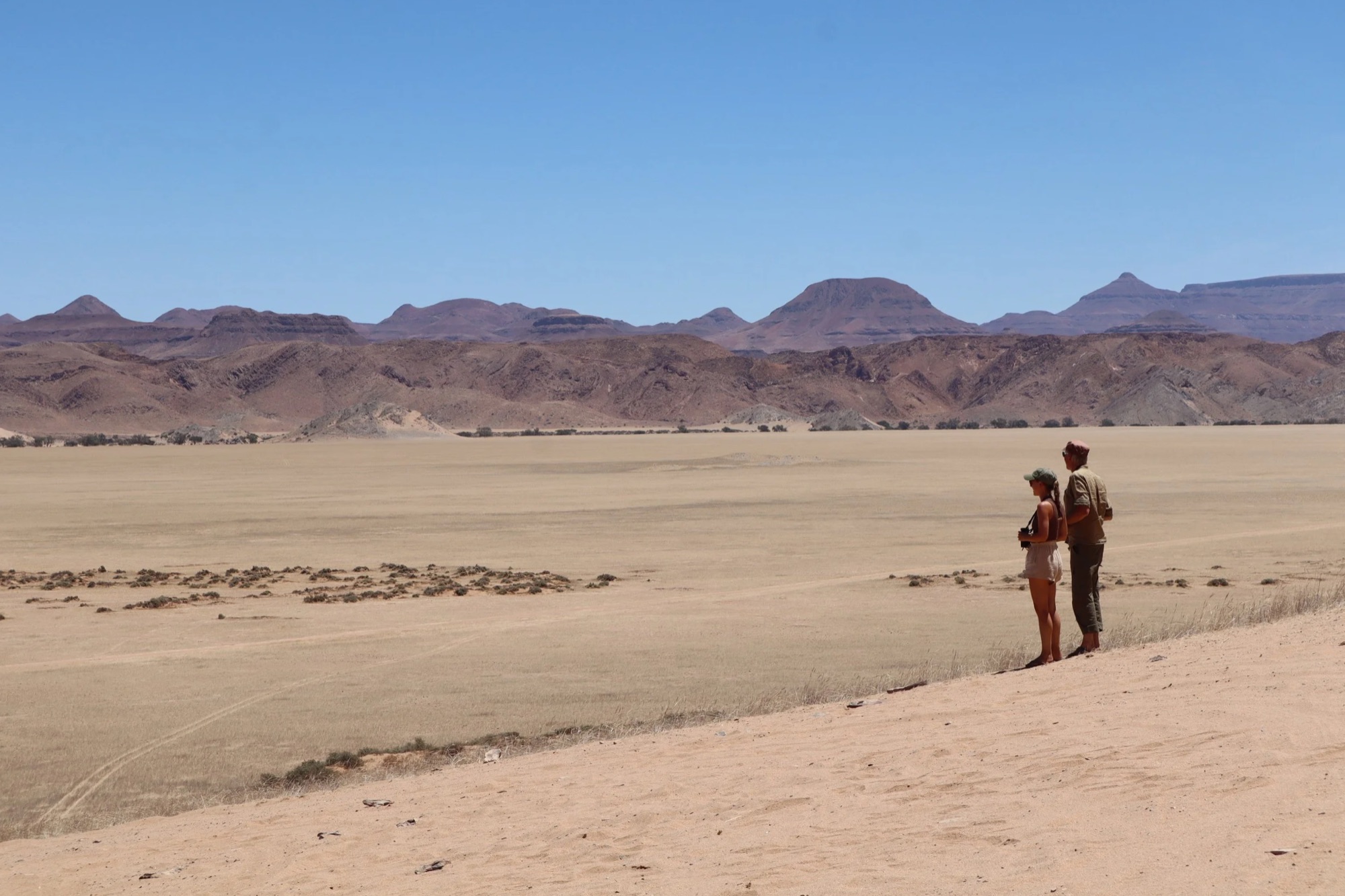 Twee reizigers kijken uit over een weidse woestijnvlakte met bergen in Namibië